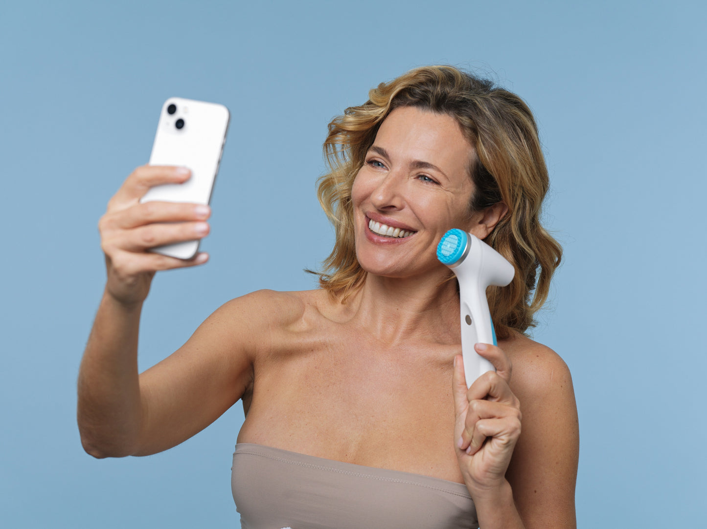 Woman with ageLOC LumiSpa iO in hand looks into her cell phone